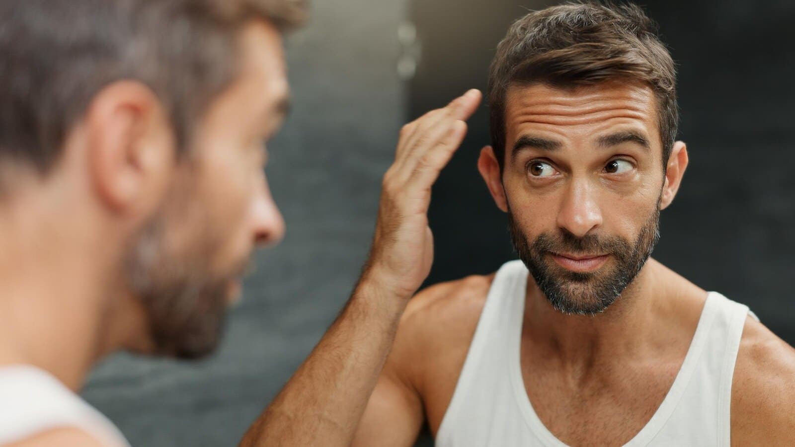 Man styling short hair in a bathroom mirror for more natural volume