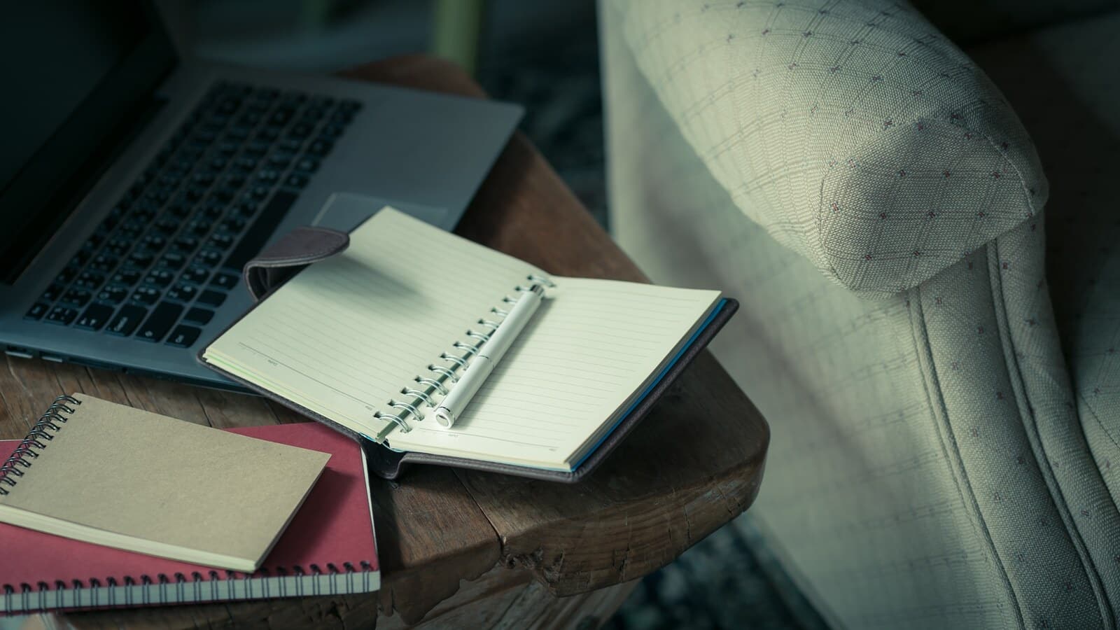 Writer planning a horror blog on a laptop with a notebook on a dark desk