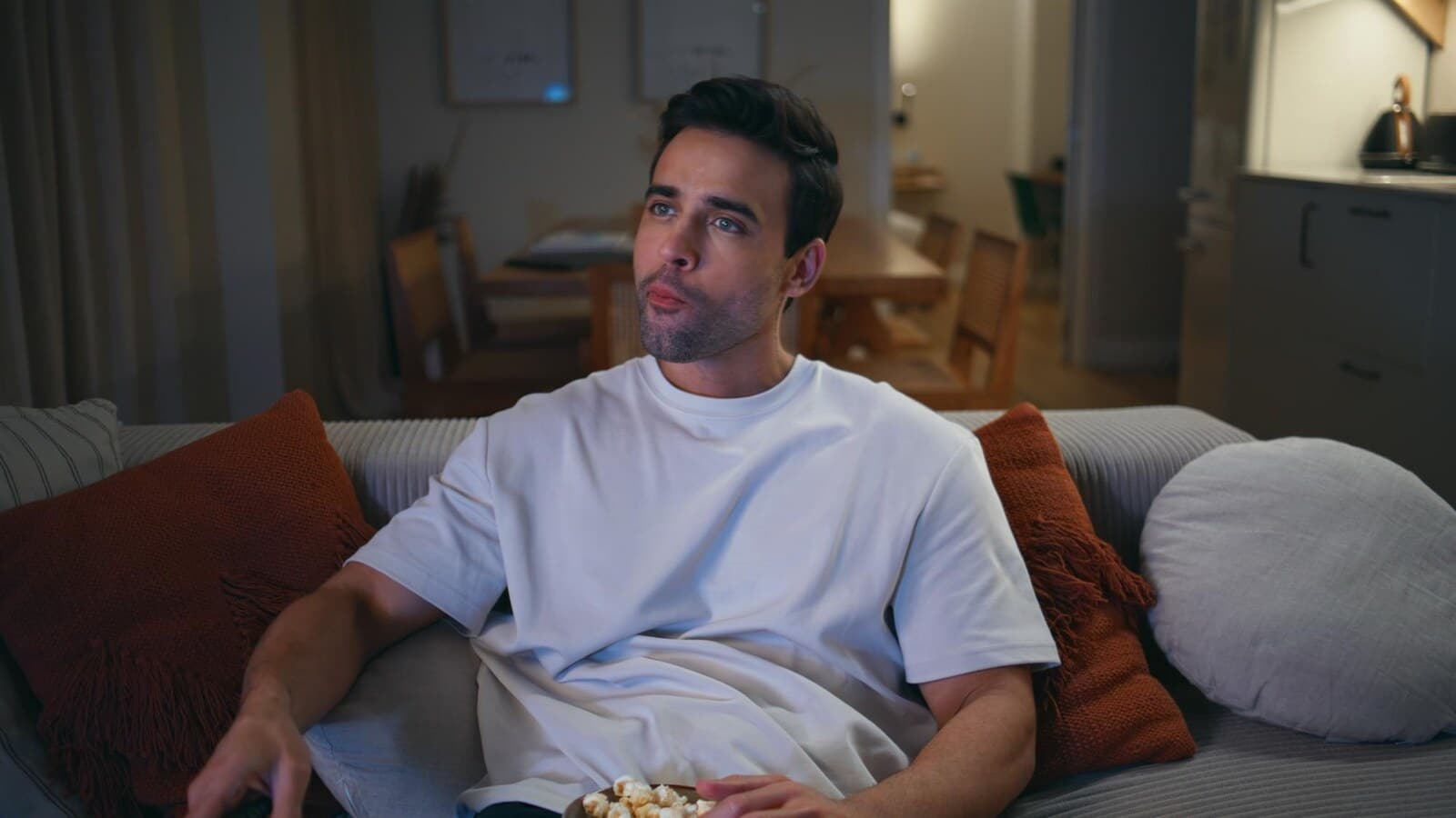 Man in a casual shirt watching a scary movie on a couch at night