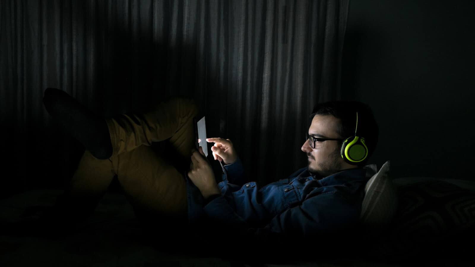 Person wearing headphones while watching a scary movie in a dark room