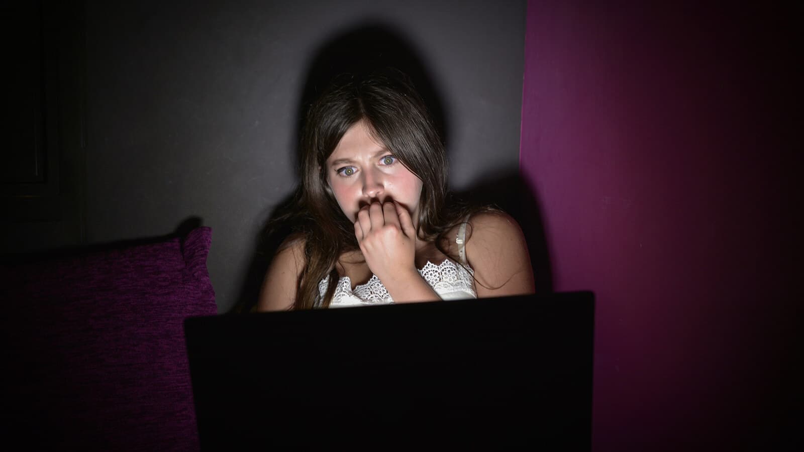 Person startled while watching a scary movie on a laptop in a dark room