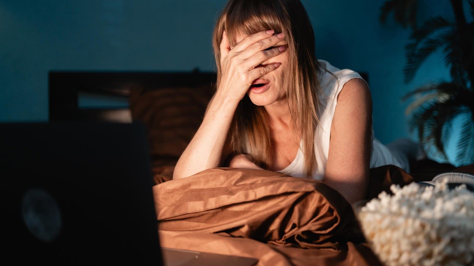Person watching a scary movie in bed at night with a laptop glow